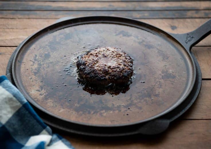Process shot showing how to cook burgers in a cast iron skillet.