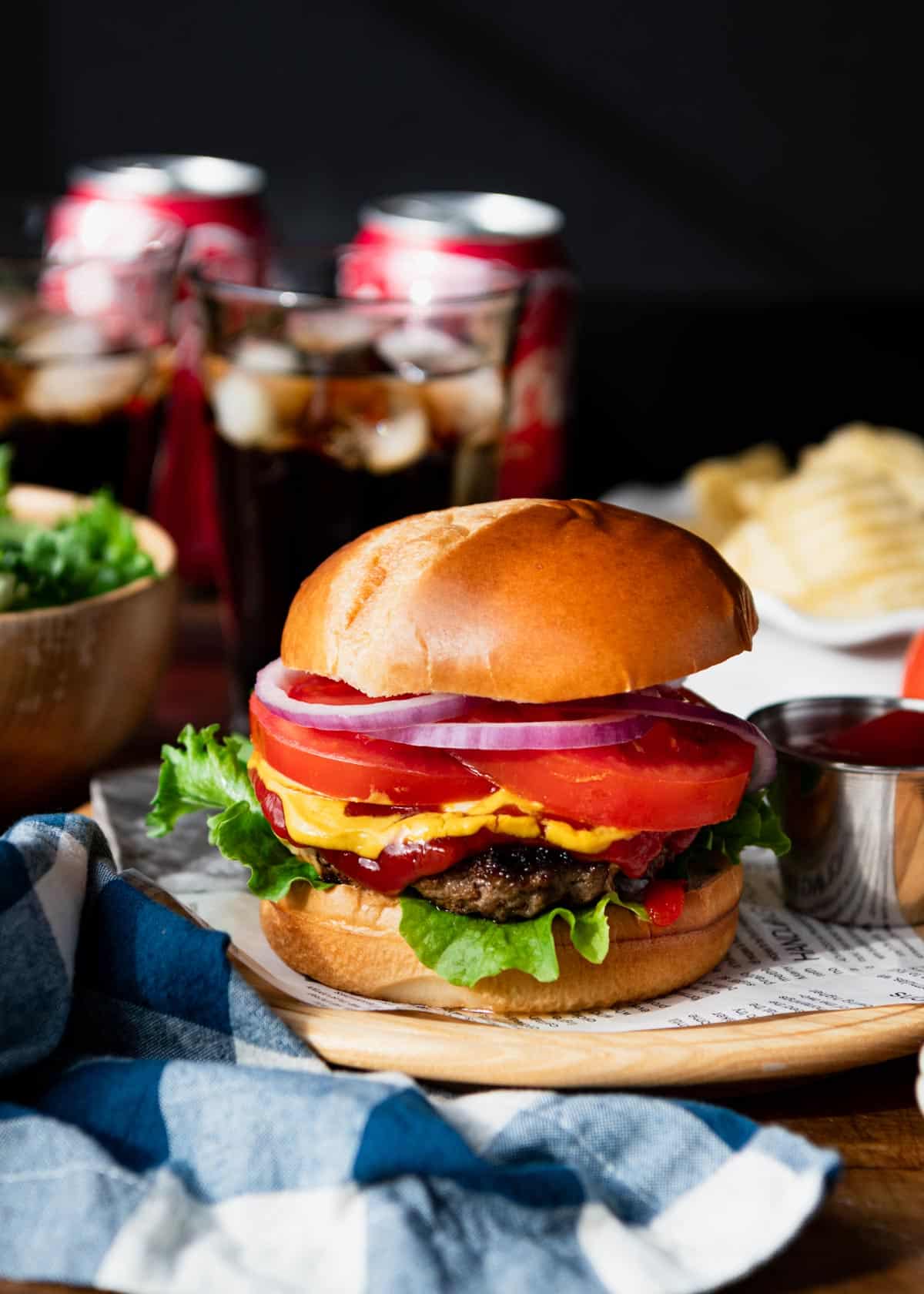 Skillet burgers on a wooden plate with chips and coke in the background.