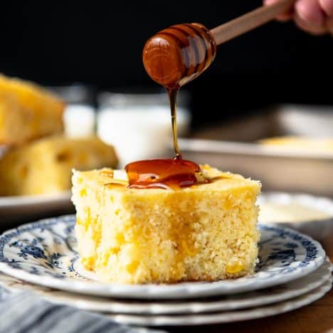 Square side shot of drizzling honey on a slice of cornbread with corn.