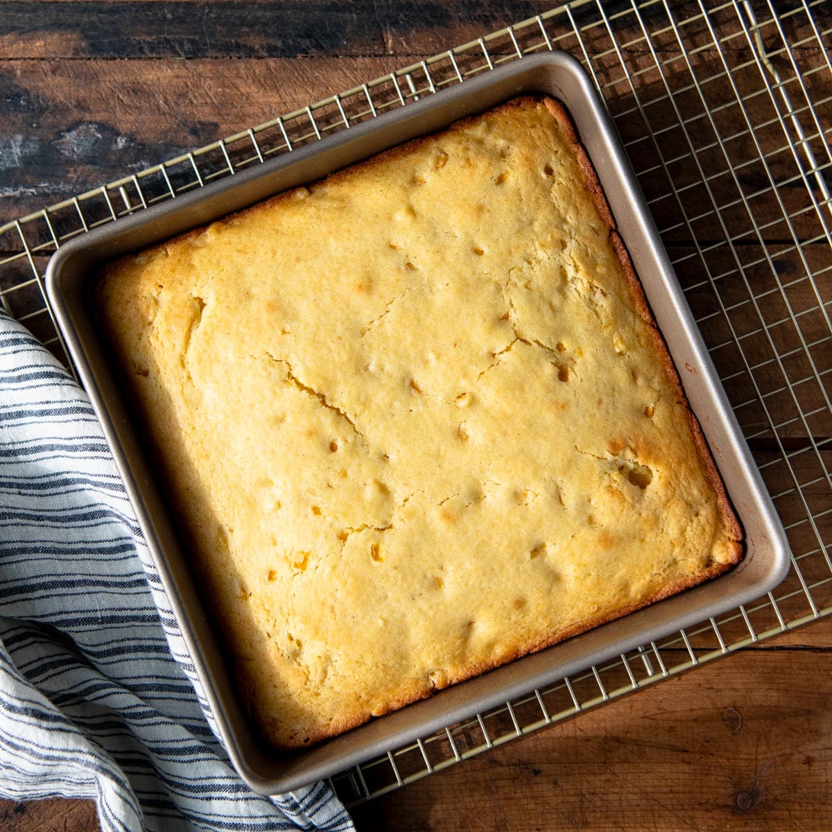Overhead shot of cornbread with corn in a square baking dish on a cooling rack.