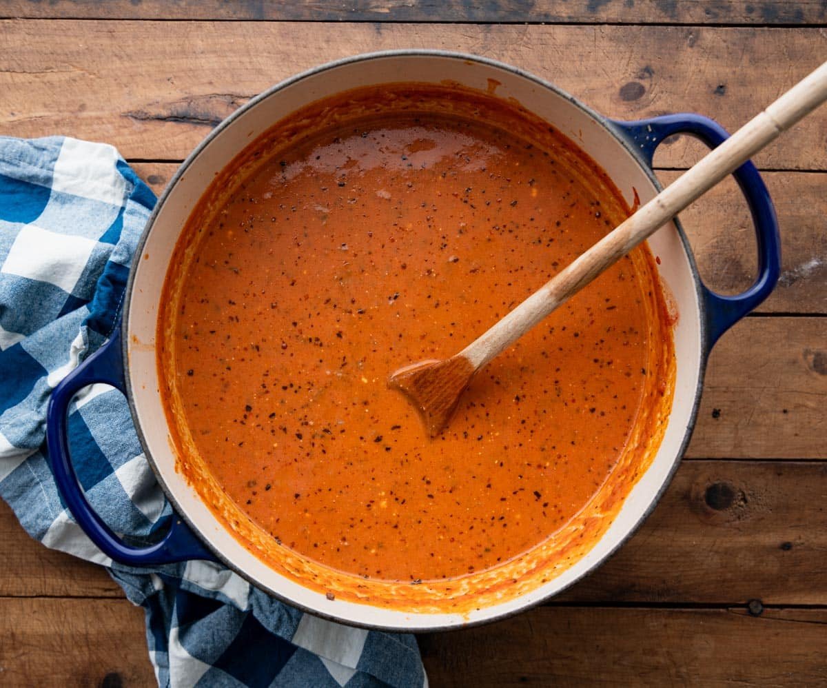 Overhead shot of a Dutch oven full of creamy beef tomato soup on a wooden table.