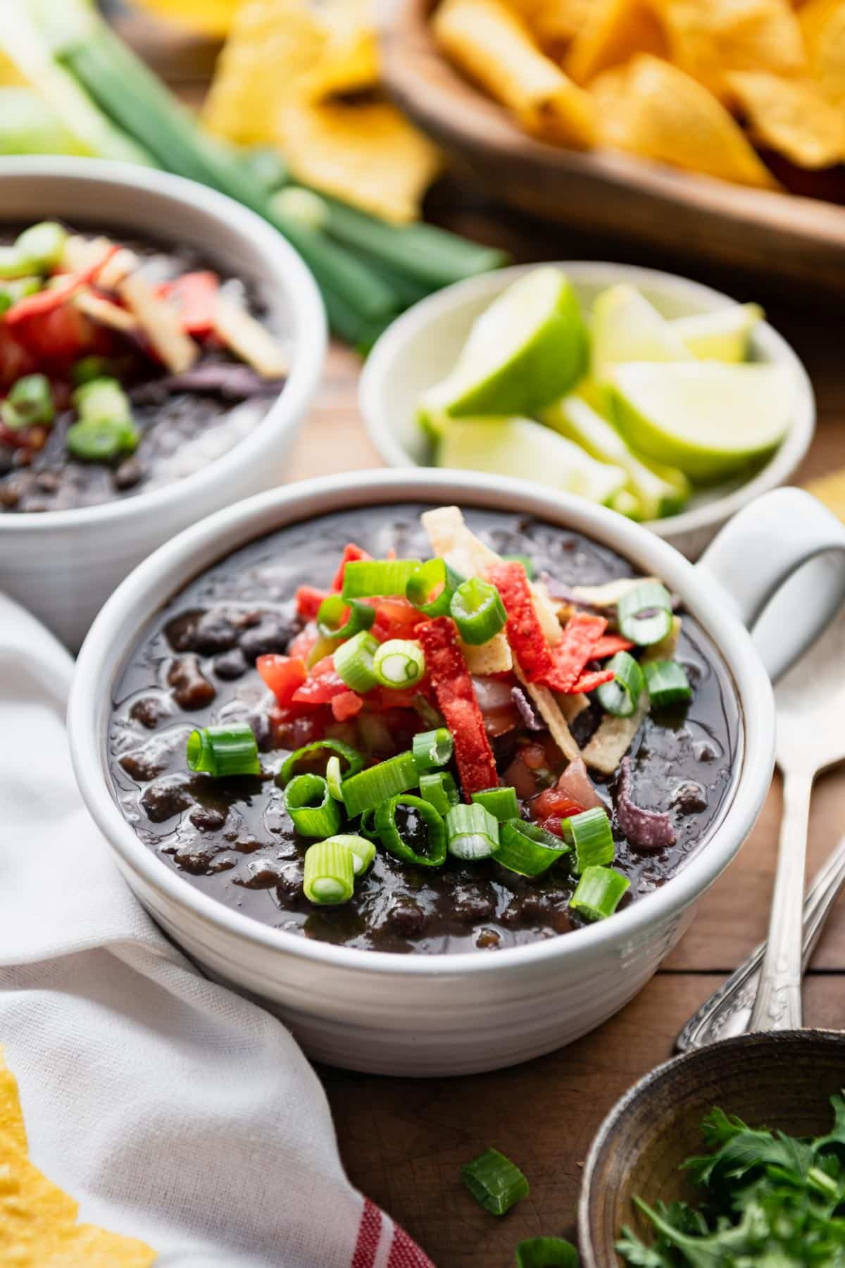 Two bowls of vegan black bean soup on a dinner table with toppings.
