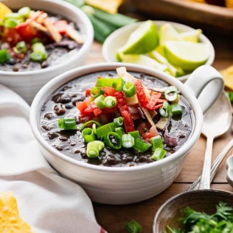 Square side shot of the best black bean soup recipe served in white bowls on a table with chips.