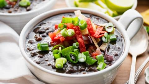 Square side shot of the best black bean soup recipe served in white bowls on a table with chips.