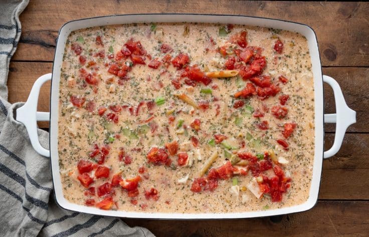 Ingredients for buffalo chicken pasta in a dish on a wooden table before baking.