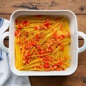 Noodles and red bell pepper in a white baking dish.