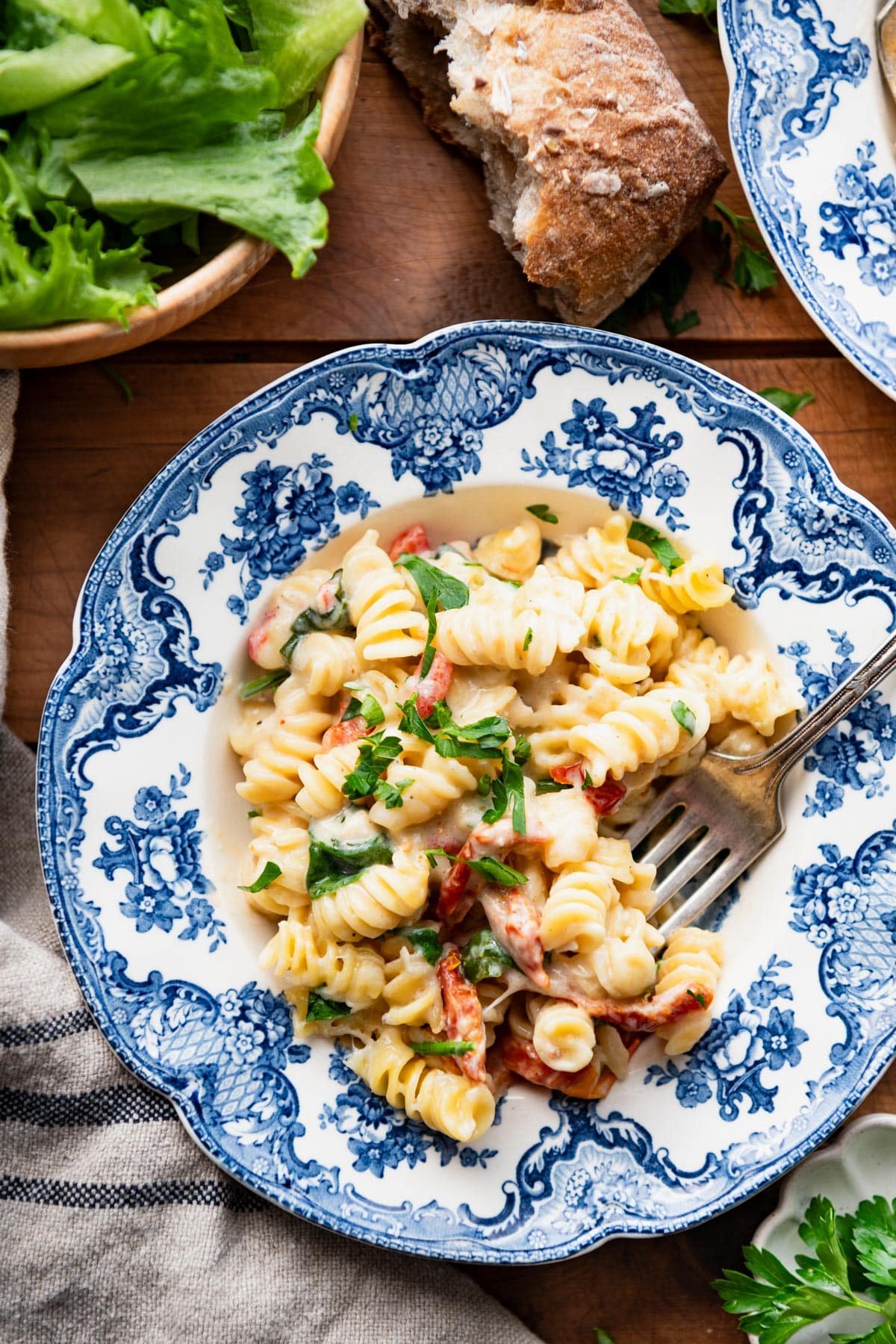 Overhead image of creamy tuscan chicken pasta in a blue and white bowl on a wooden table.