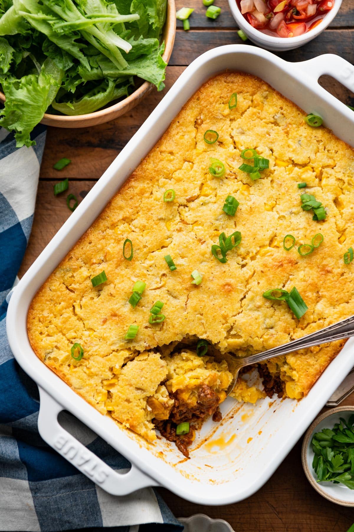 Overhead image of a serving spoon in a white dish full of an easy cornbread taco bake.
