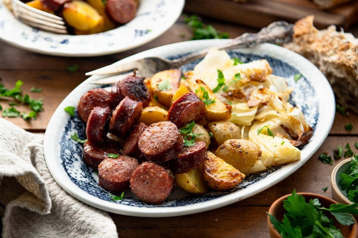 Horizontal image of a blue and white platter of sausage cabbage and potatoes.