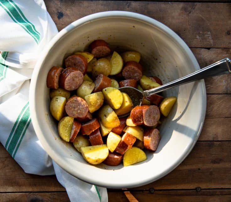 Tossing together potatoes and sausage with olive oil and seasoning.