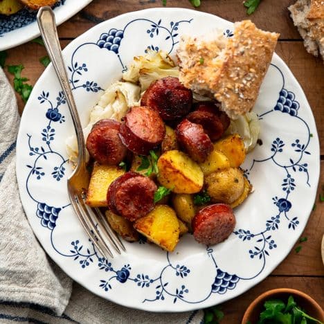 Square overhead image of cabbage potatoes and sausage in a blue and white bowl on a wooden table.