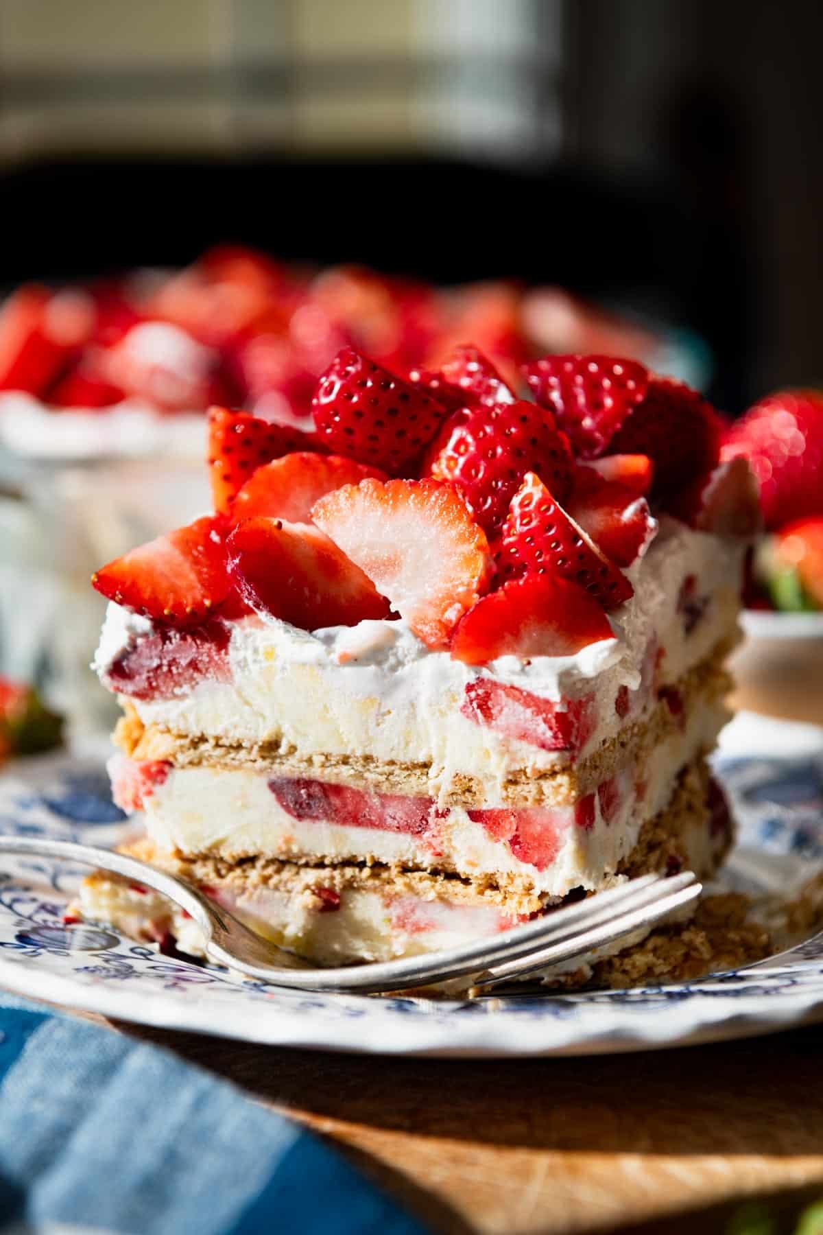 Close up side shot of a triple layer strawberry icebox cake slice on a plate.