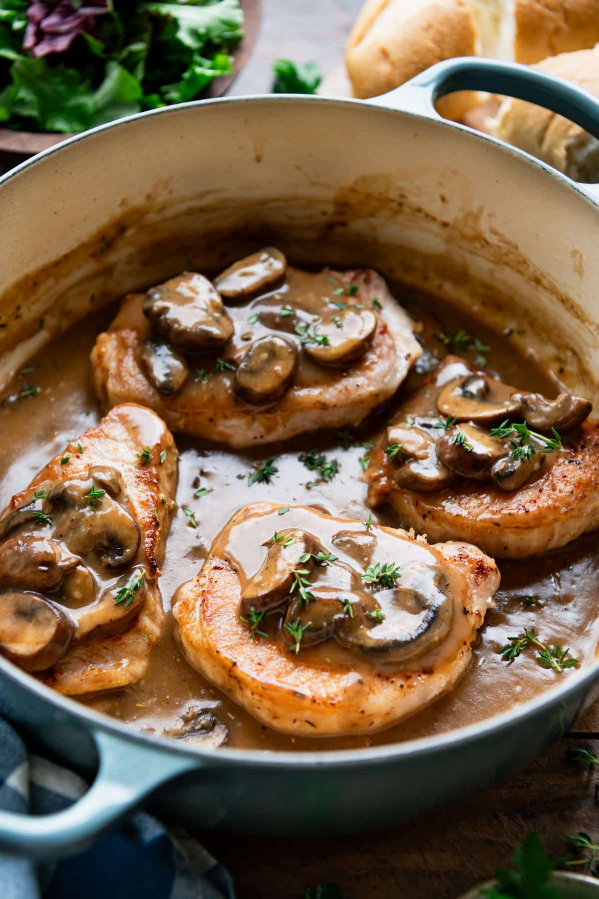 Side shot of dutch oven pork chops with mushroom gravy and fresh thyme on top.