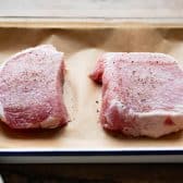 Raw thick boneless pork chops on a parchment lined tray.