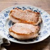 Seared thick cut boneless pork chops resting on a blue and white plate.