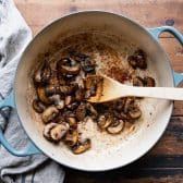 Wooden spoon sauteing mushrooms in a dutch oven.