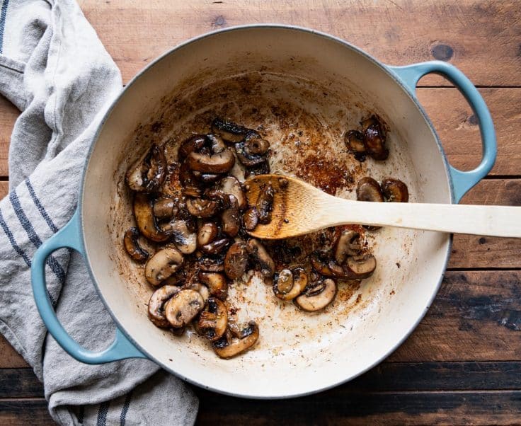 Wooden spoon sauteing mushrooms in a dutch oven.