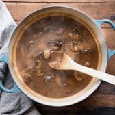 Wooden spoon stirring mushroom gravy in a dutch oven.