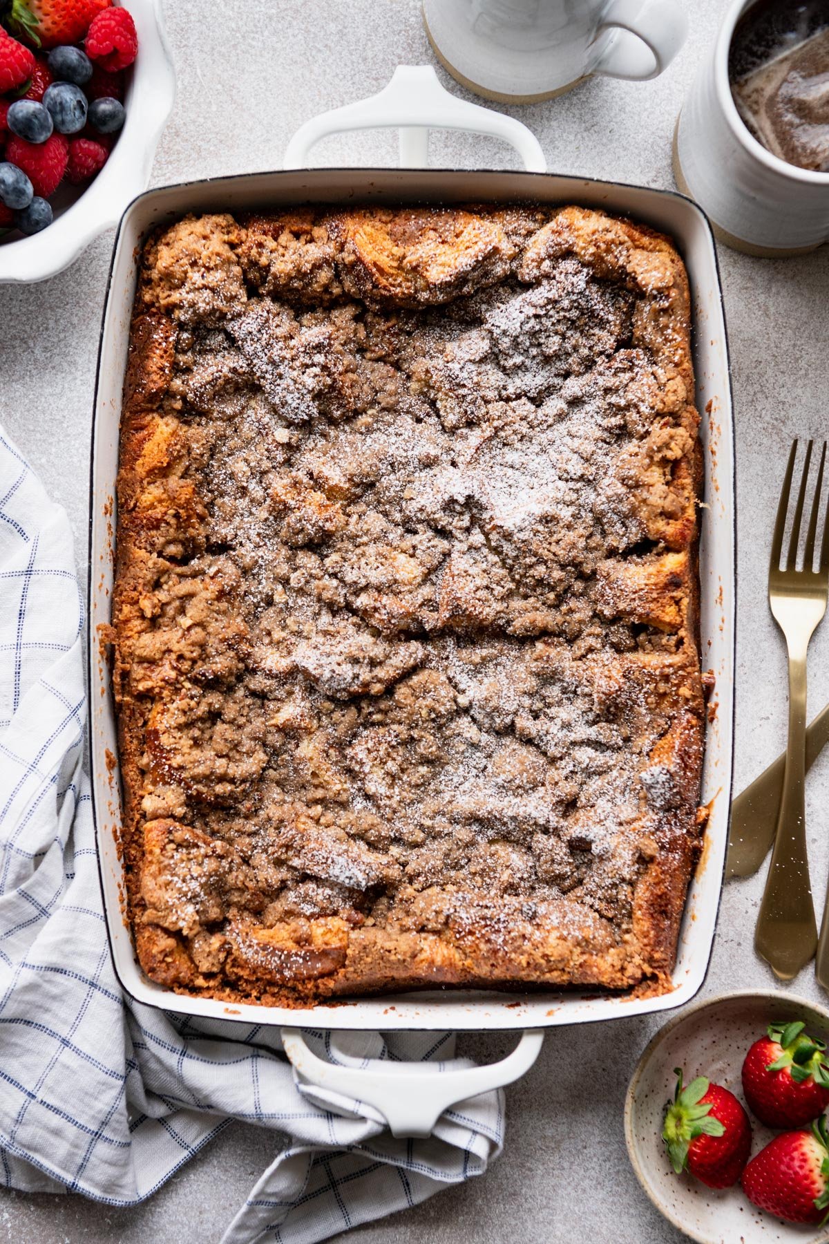 Brioche french toast casserole with streusel topping baked in a white dish and dusted with powdered sugar.