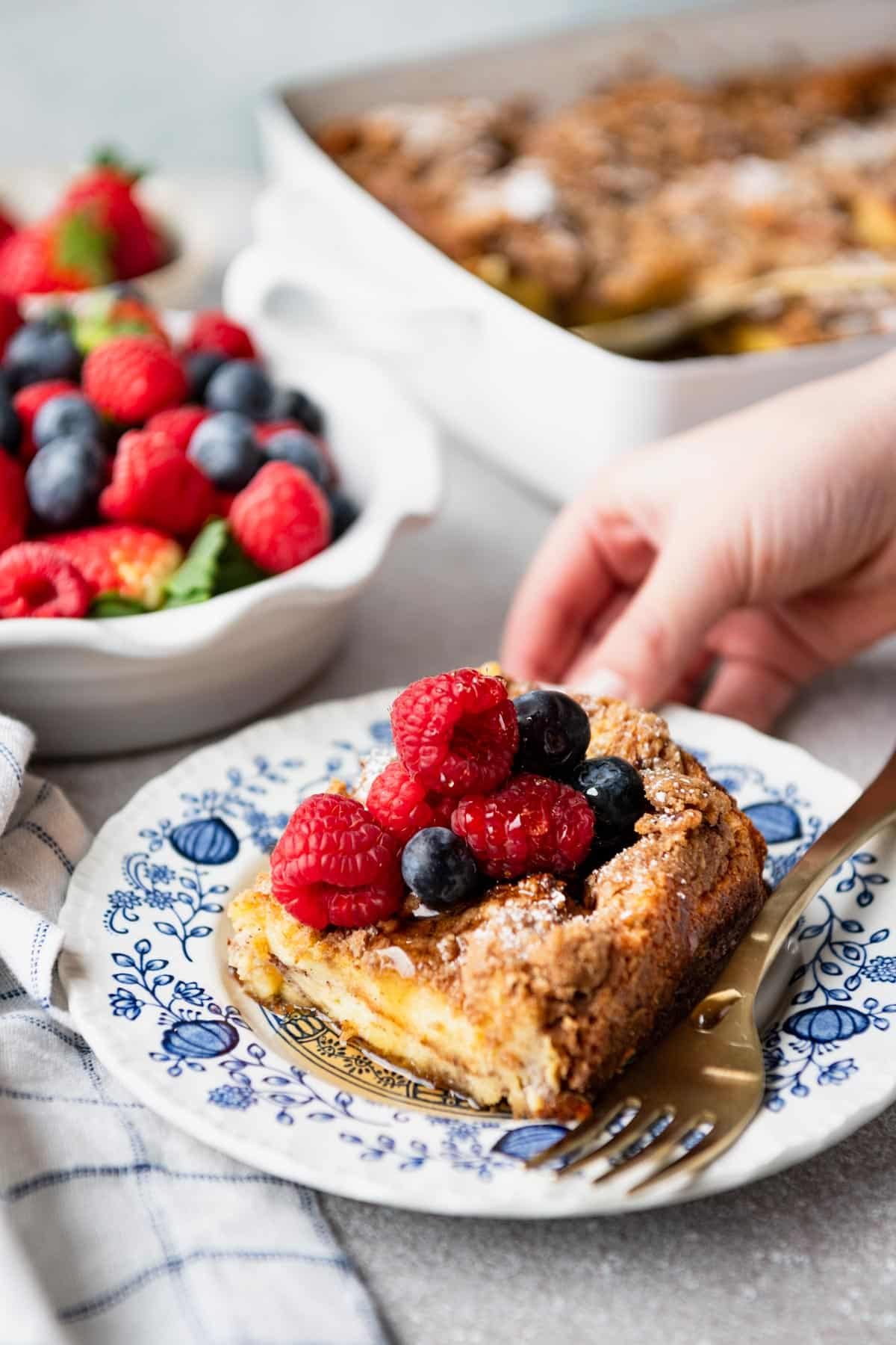 Child's hand holding a blue and white plate with brioche french toast casserole.