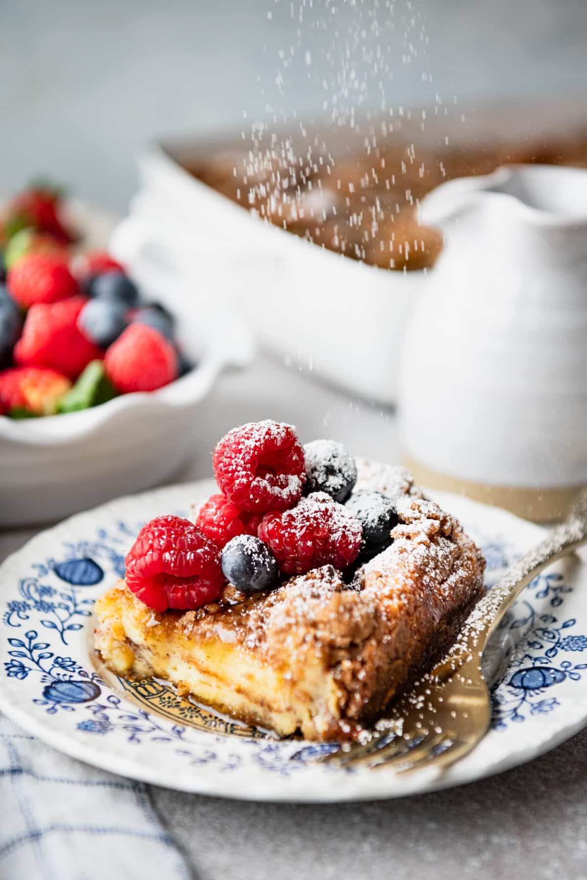 Piece of easy brioche french toast casserole on a plate with powdered sugar and fresh berries.