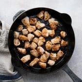 Browning diced chicken in a cast iron skillet.