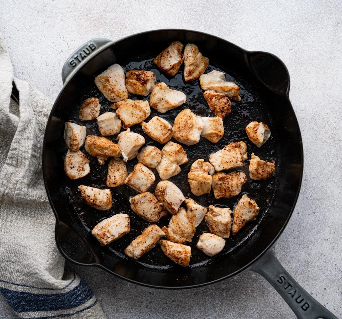 Browning diced chicken in a cast iron skillet.