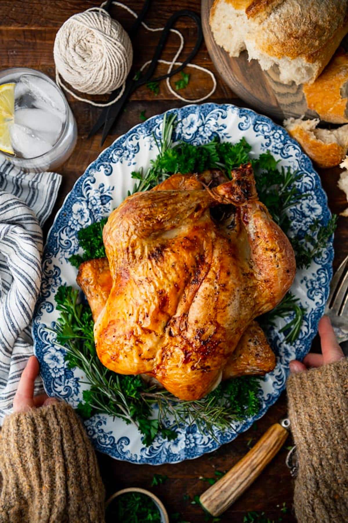 Overhead shot of hands holding a blue and white platter with a Dutch oven chicken on it.