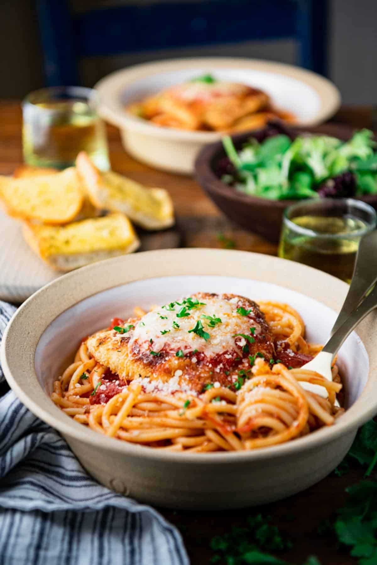 Two bowls of the best chicken parm recipe served with wine and salad and bread.