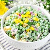 Square image of english pea salad in a white bowl with fresh flowers in the background.