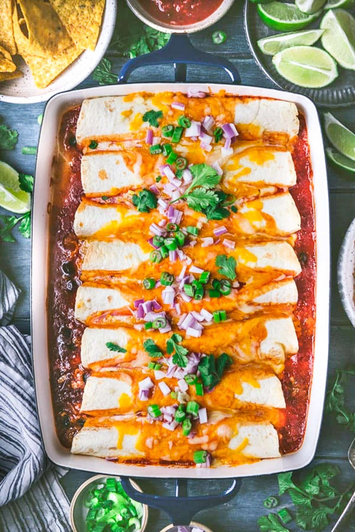 Overhead image of ground beef enchiladas in a baking dish with green onions, red onions, and cilantro on top.