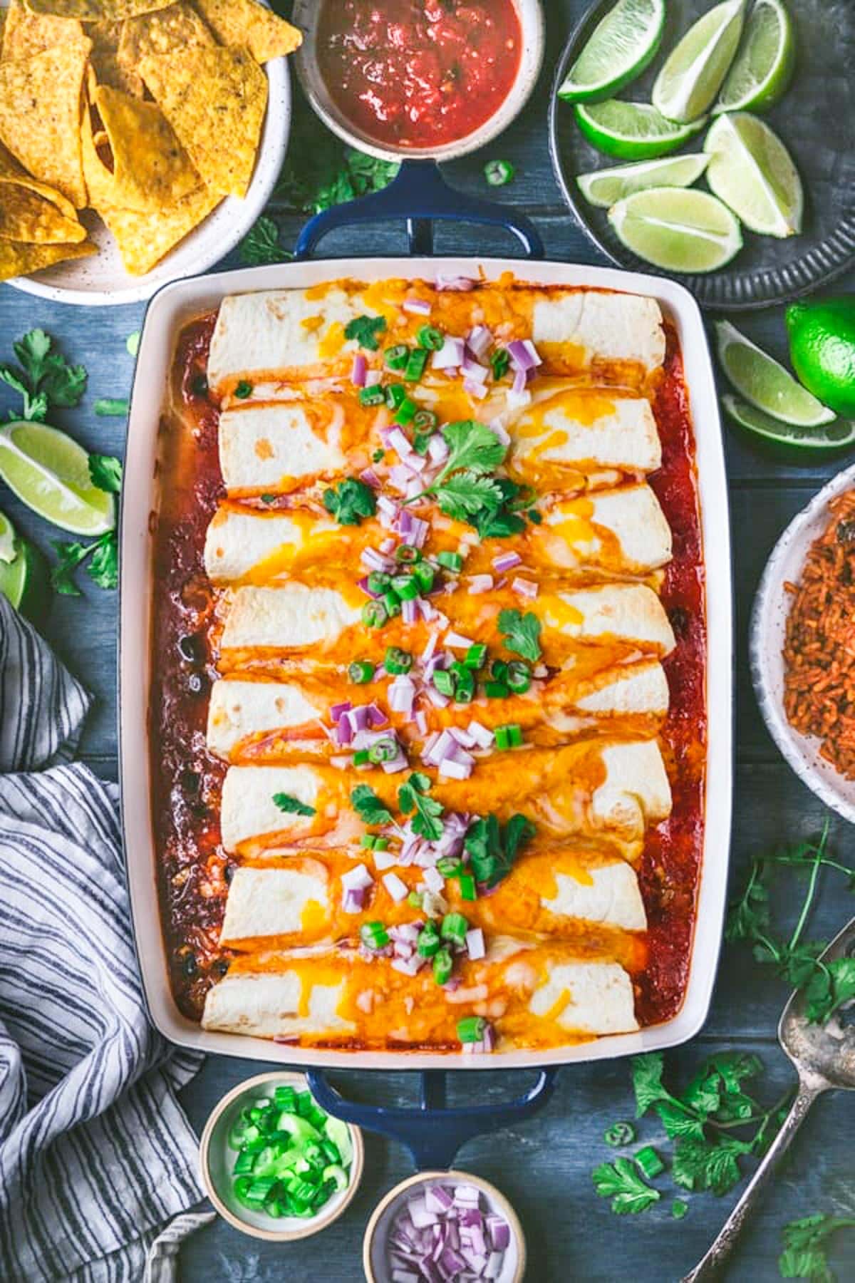 Overhead shot of ground beef enchiladas in a baking dish on a blue table.