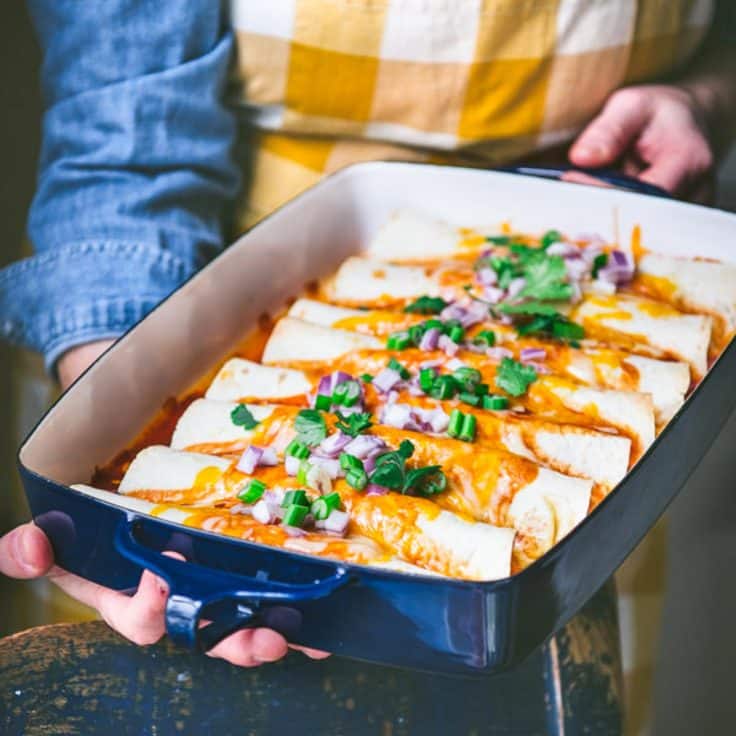 Square side shot of hands holding a tray of easy ground beef enchiladas.