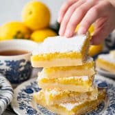 Hands picking up a bar from a stack of old fashioned lemon squares.