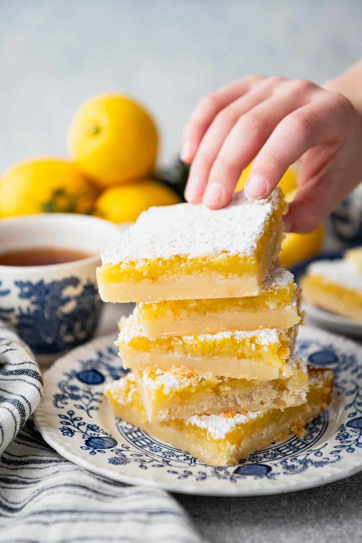 Hands picking up a bar from a stack of old fashioned lemon squares.