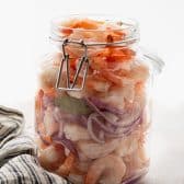 Shrimp, red onions, and bay leaves layered in a large glass jar.