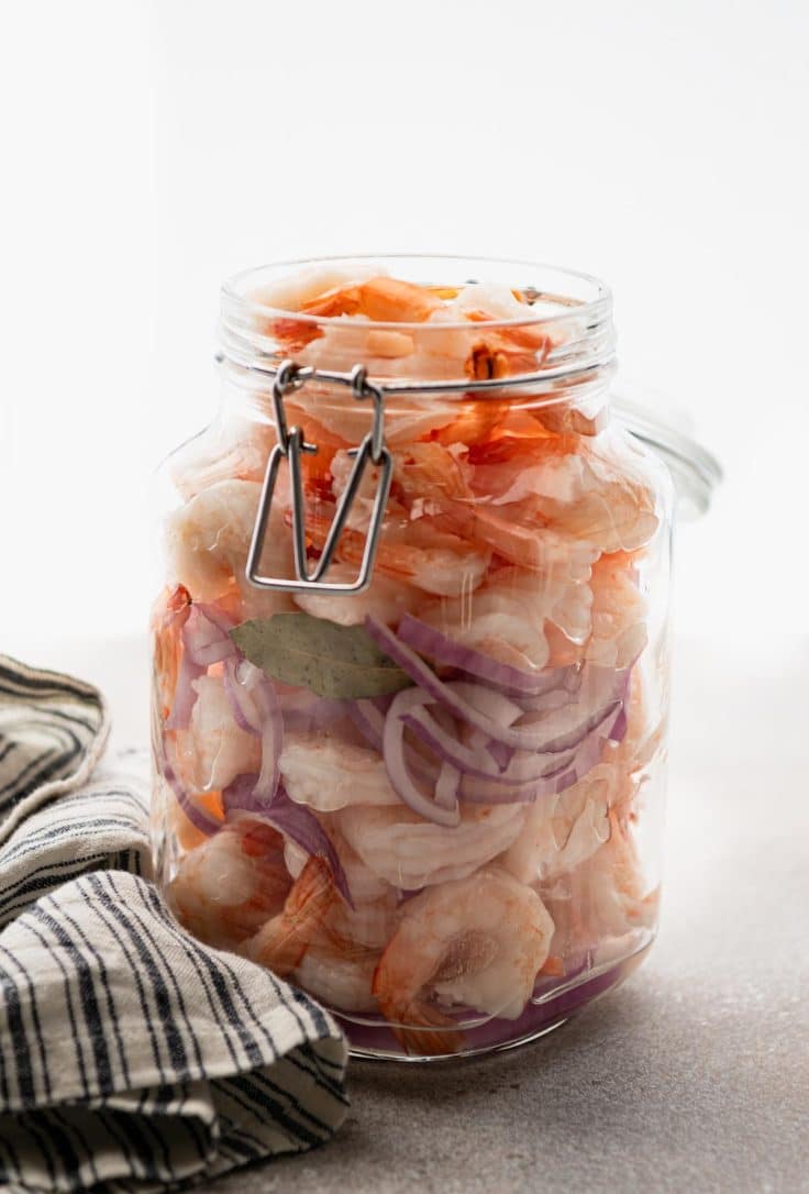 Shrimp, red onions, and bay leaves layered in a large glass jar.