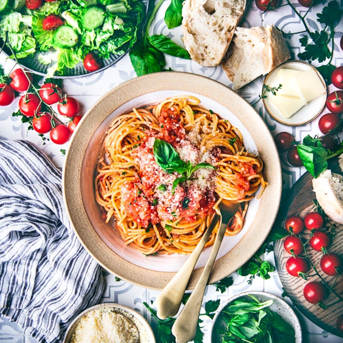 Square overhead image of pomodoro sauce on a bed of pasta in a bowl with a salad and bread on the side.