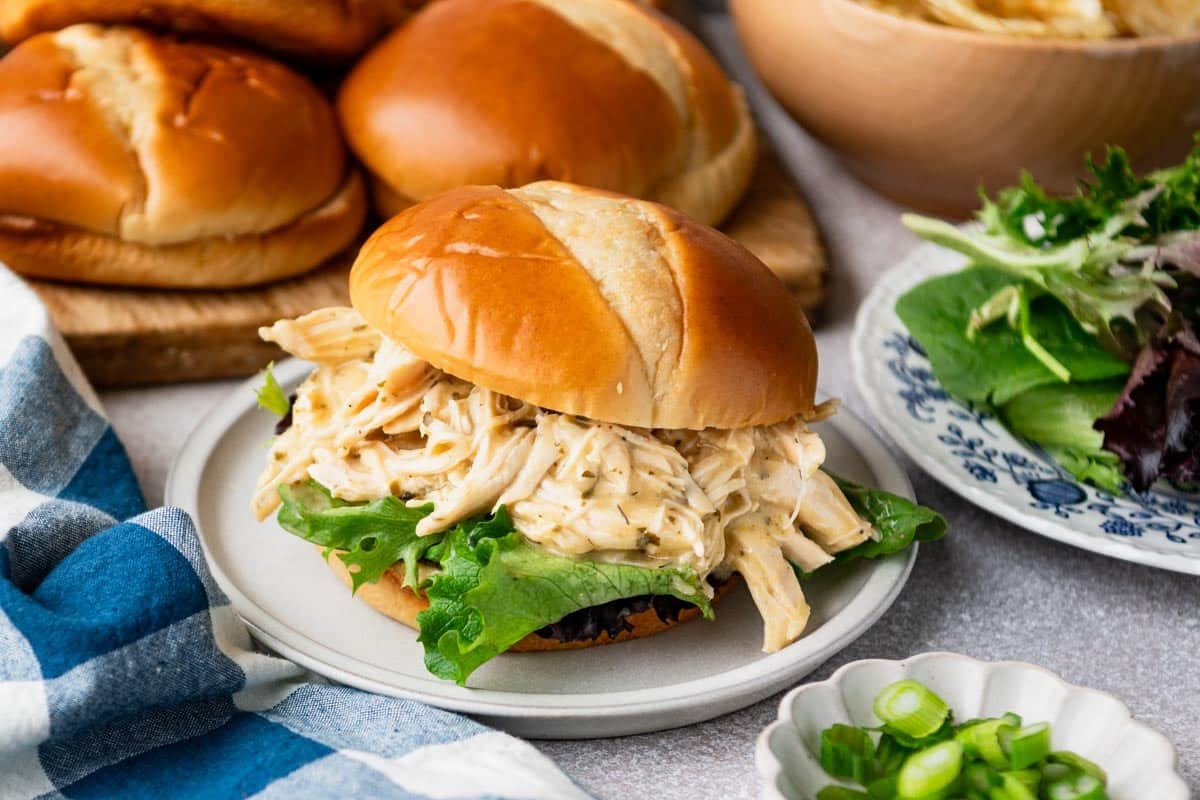 Horizontal side shot of a shredded slow cooker ranch chicken sandwich on a plate.
