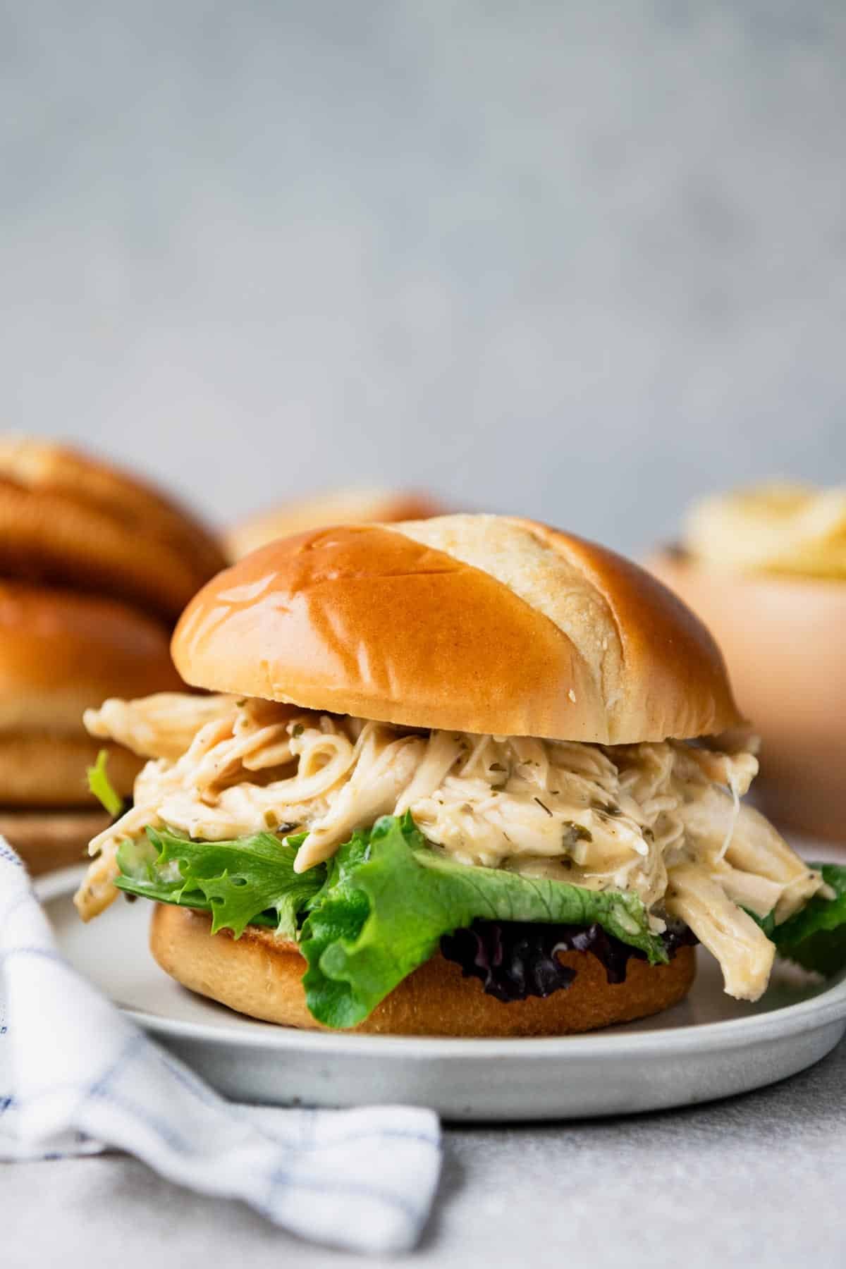 Shredded ranch chicken crock pot recipe served on a brioche bun with chips in the background.