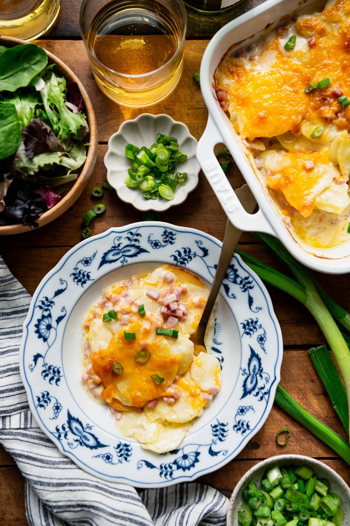 Overhead shot of scalloped potatoes and ham on a wooden dinner table.