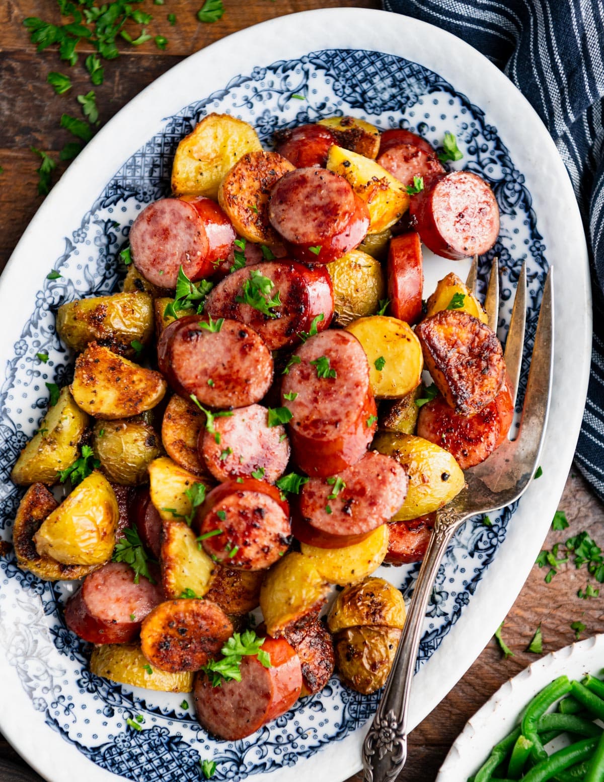 Close overhead image of smoked sausage and crispy potatoes on a blue and white platter.
