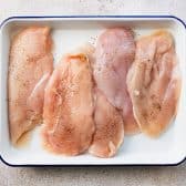 Boneless skinless chicken breast on a tray and seasoned with salt and pepper.