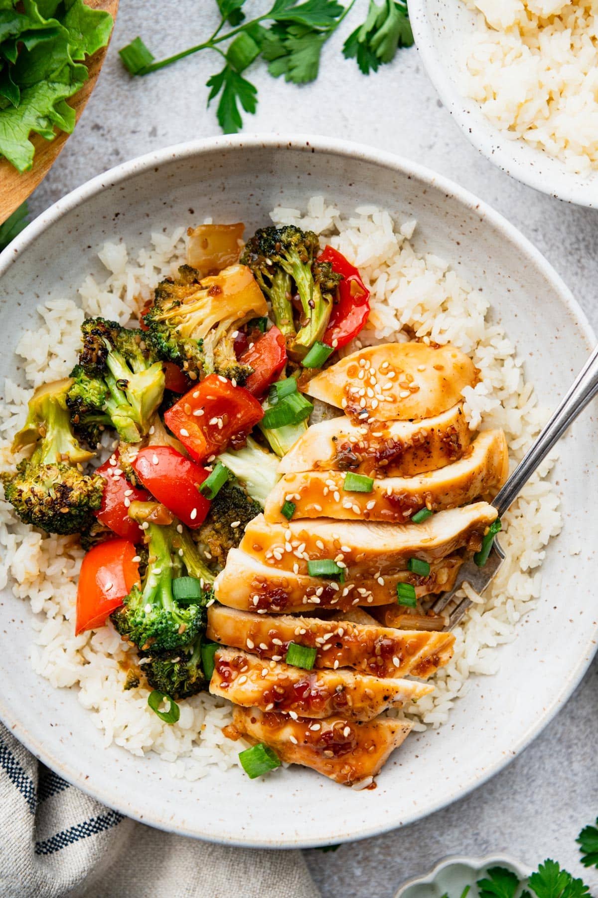 Close overhead shot of baked teriyaki chicken on a bowl of rice with broccoli and bell peppers.