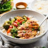 Horizontal side shot of baked teriyaki chicken in a bowl with rice and vegetables.
