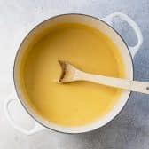 Stirring cheese sauce in a white Dutch oven.