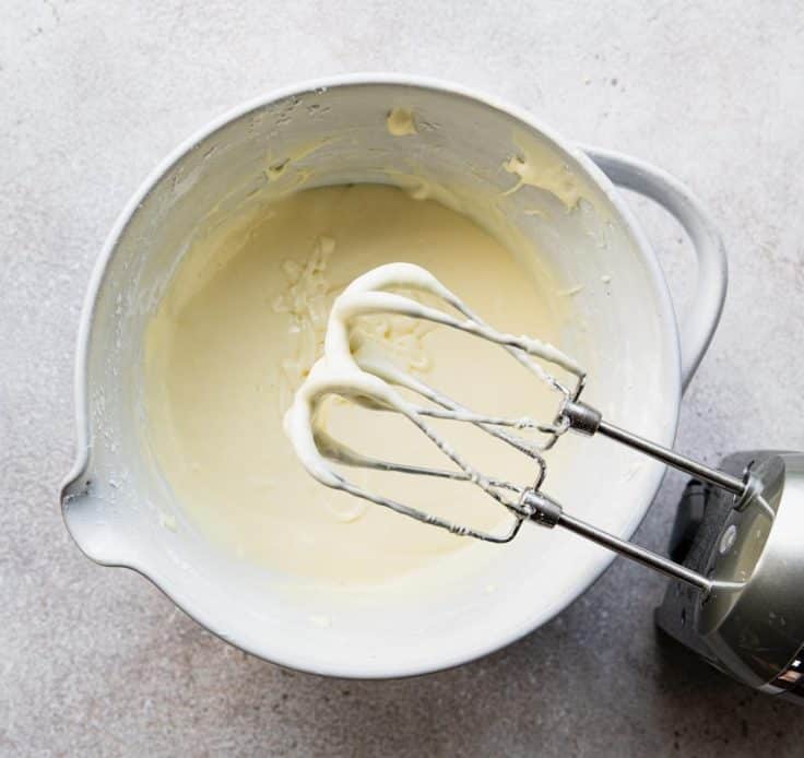 Filling for chess squares in a white mixing bowl with an electric hand mixer.