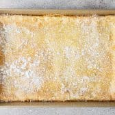 Overhead shot of a pan of chess bars dusted with powdered sugar before slicing.