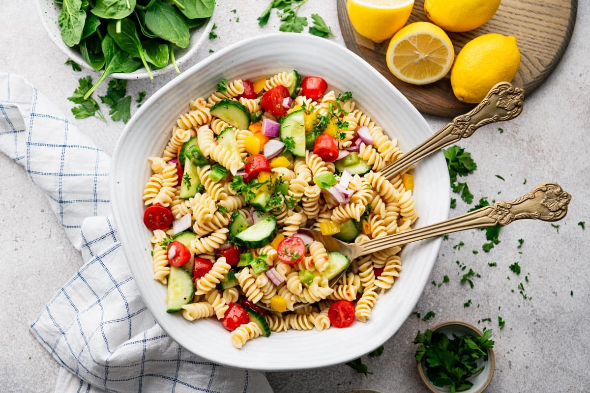 Horizontal overhead image of a bowl of classic pasta salad on a white table.