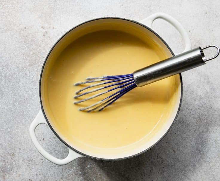 Whisking cheese sauce in a white Dutch oven.